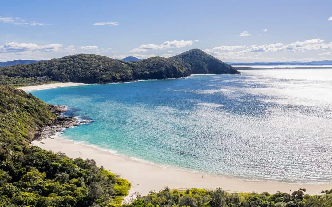 A scenic coastal view at Blueys Beach, one of the top NSW places to go for a beach escape, with clear blue waters, lush headlands, and white sandy shores.